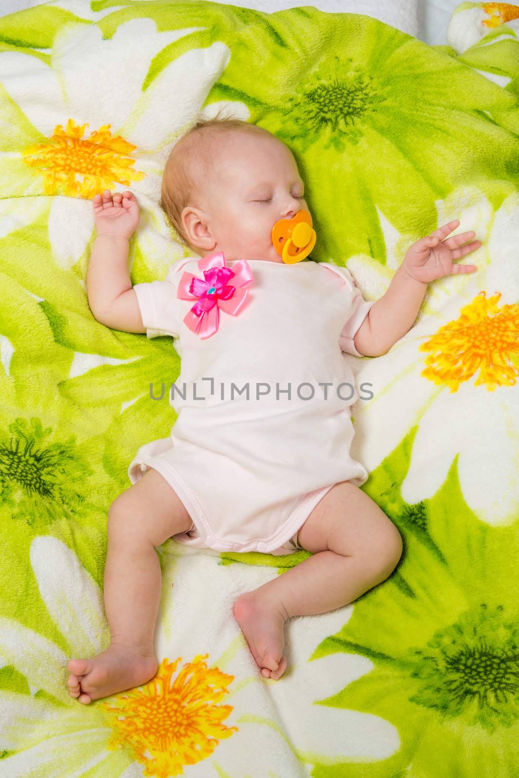 a two-month baby girl Europeans lies on a soft bed on colored coverlet