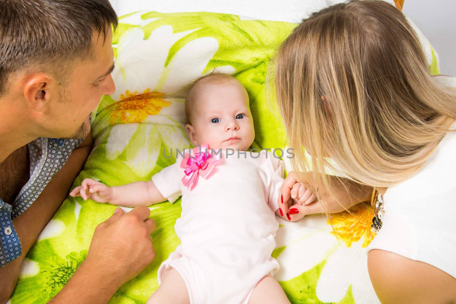 Young parents Mom and Dad sit at the crib, the crib on his back lying on the two-month girl