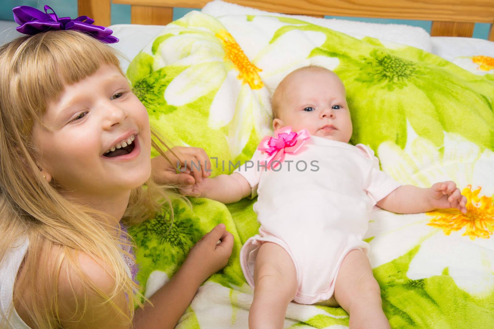 Five-year girl joyfully laughs while holding the handle of a newborn baby by Madhourse