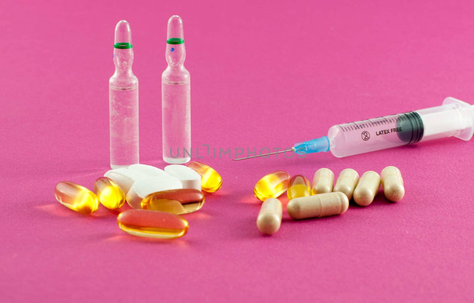 Phials, pills and syringe on pink background