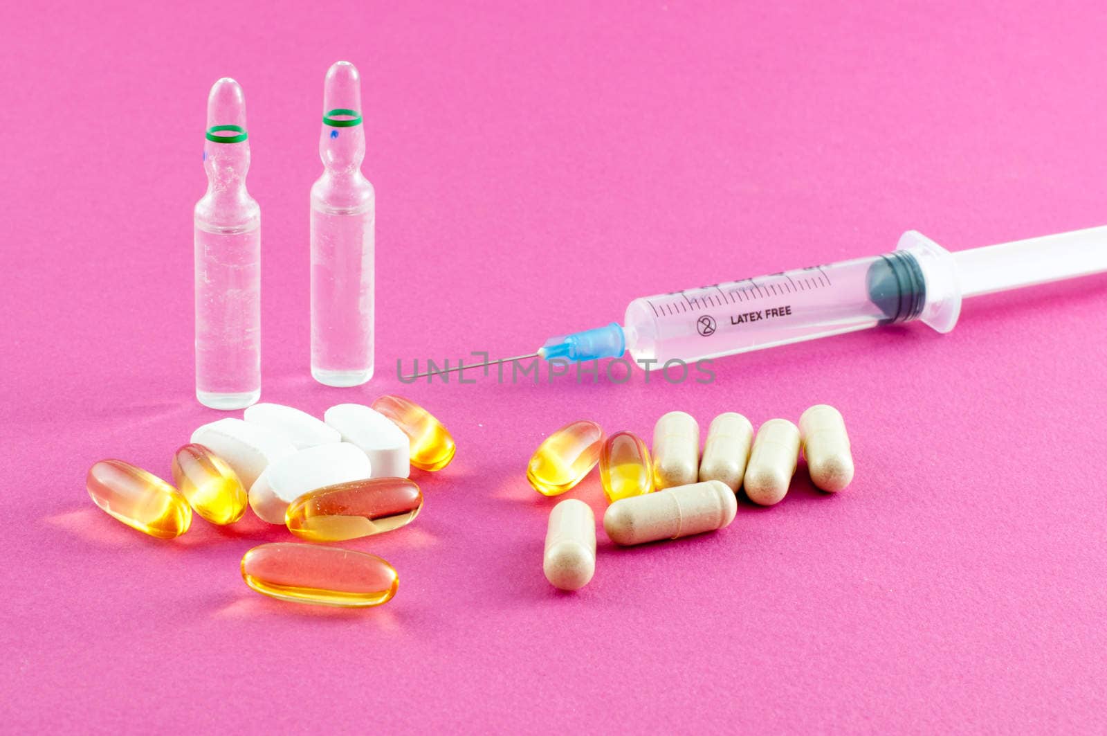 Phials, pills and syringe on pink background