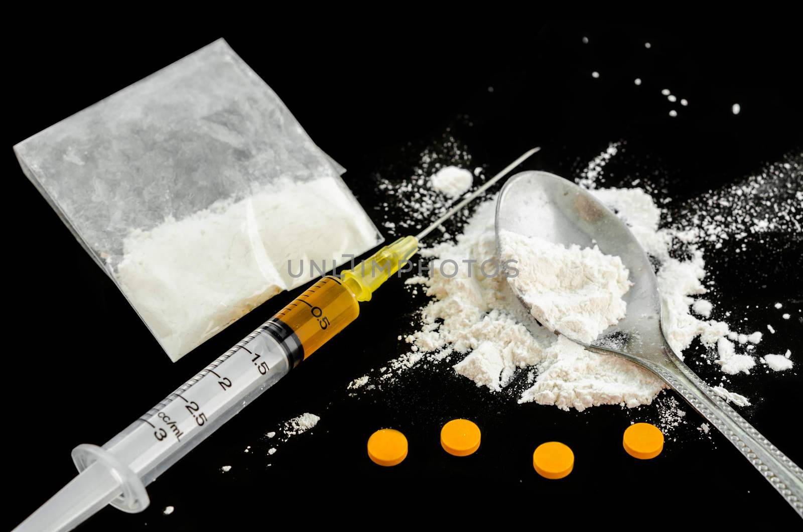 Drug syringe, amphetamine tablets and cooked heroin on spoon.