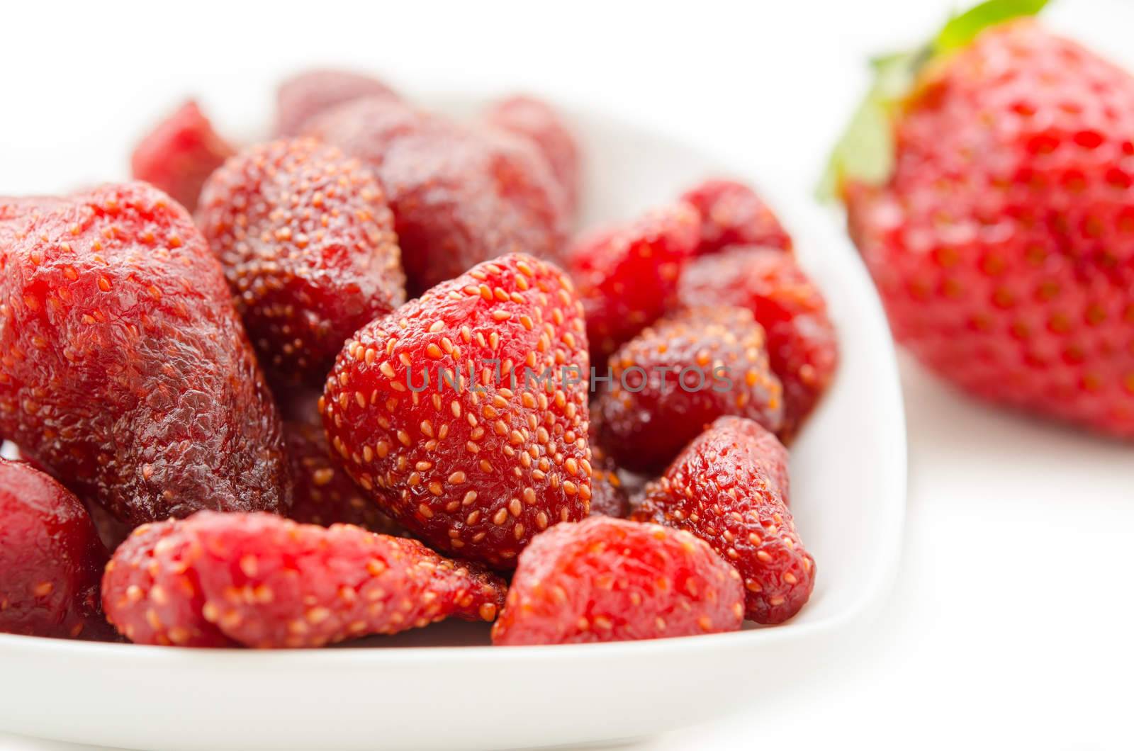 Dried strawberries in white bowl and fresh strawberry on white background.