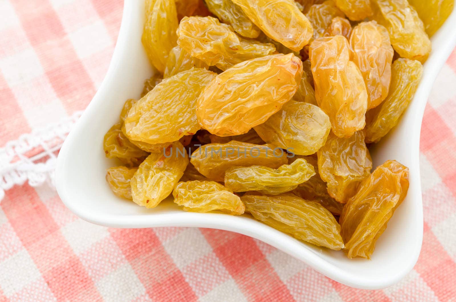 Dried Yellow raisins in white bowl on table cloth.