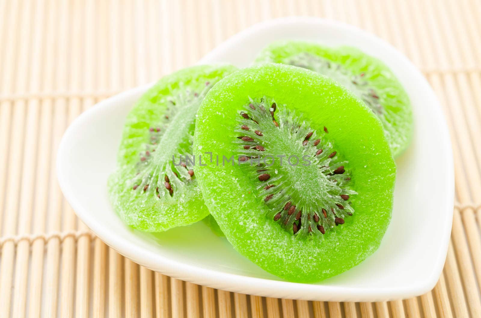 Dried kiwi in white bowl heart shape on mat background.