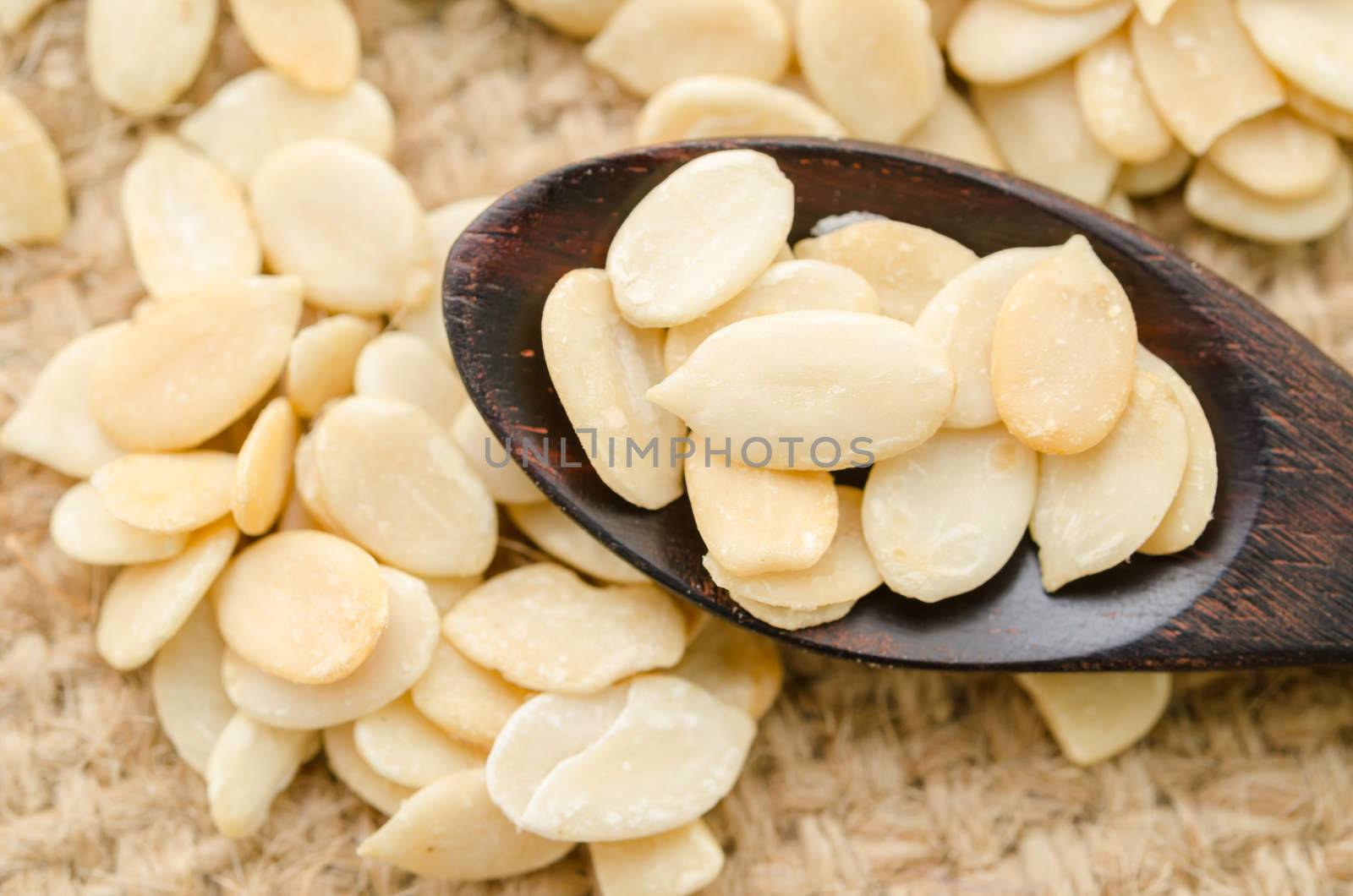 Crack shell watermelon seeds in wooden spoon on sack background.