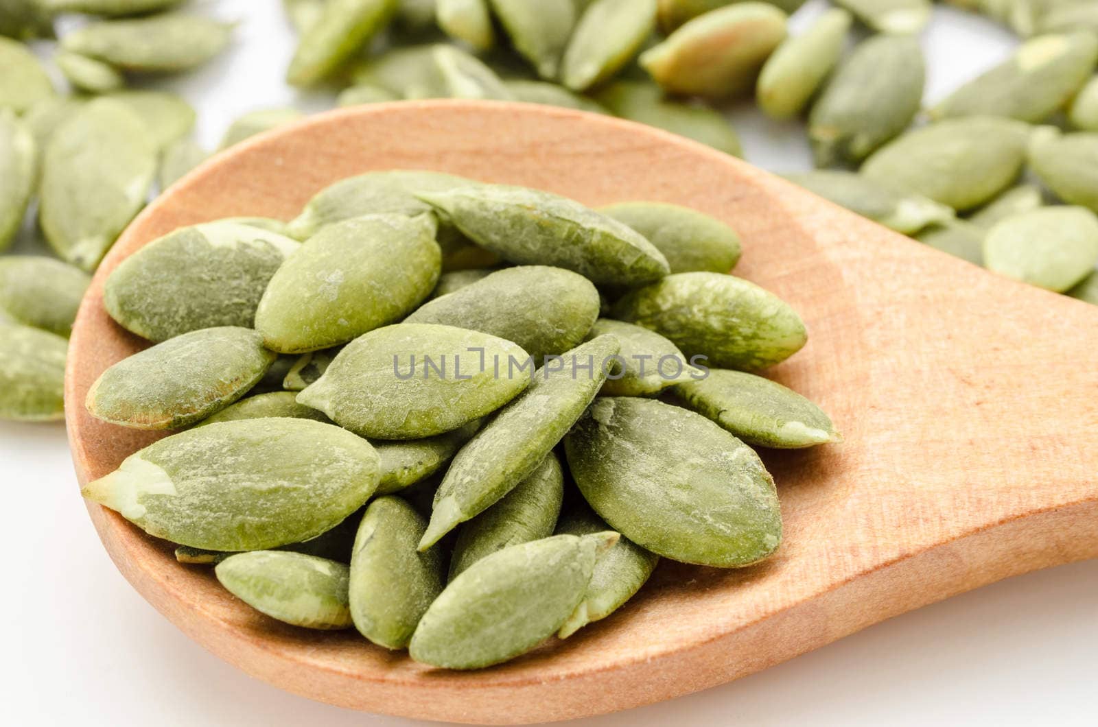 Dried Pumpkin Seeds in wooden spoon on white background.