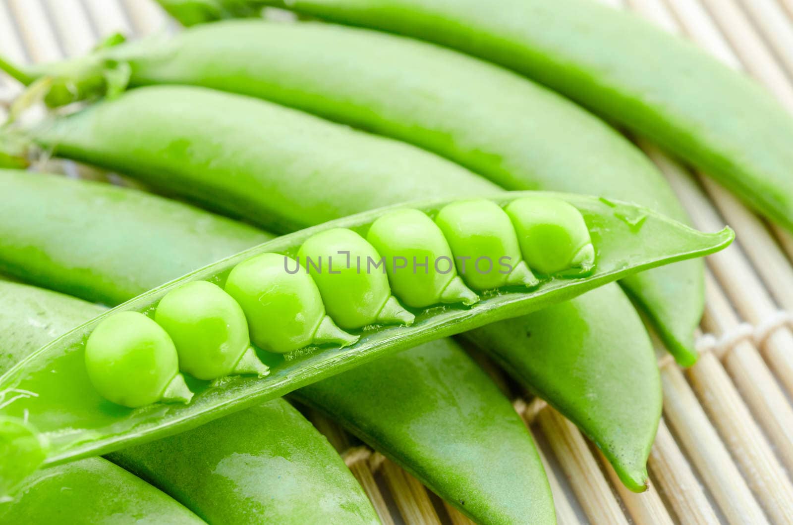 Fresh green peas pods on bamboo mat background.