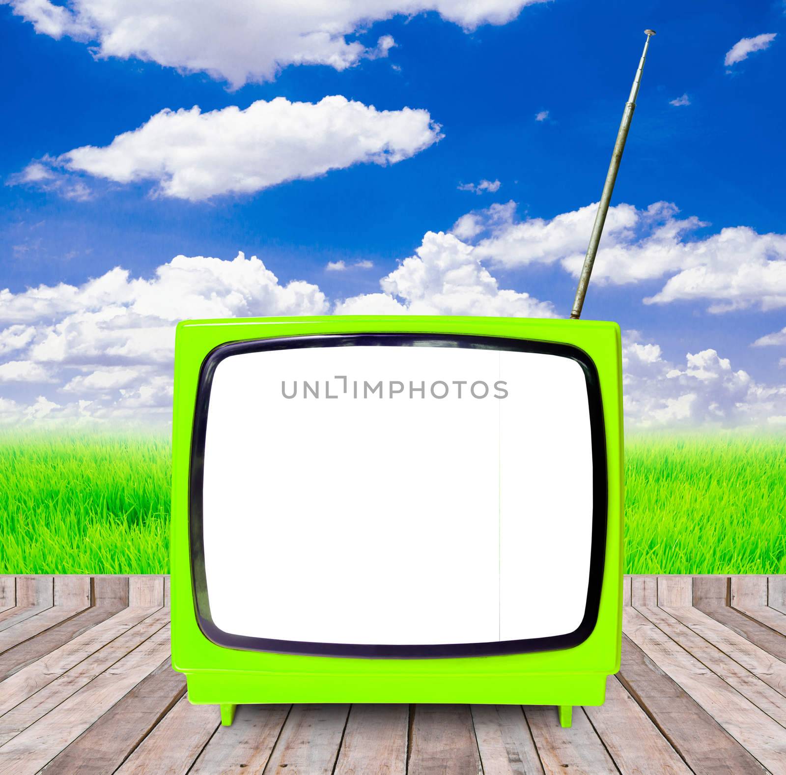 Photo of an old retro TV outdoors on wooden with blue sky and white clouds in the background.