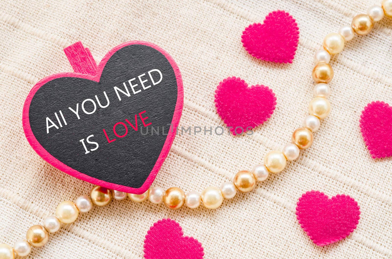 All you need is love on pink heart wooden clamps and on fabric background.