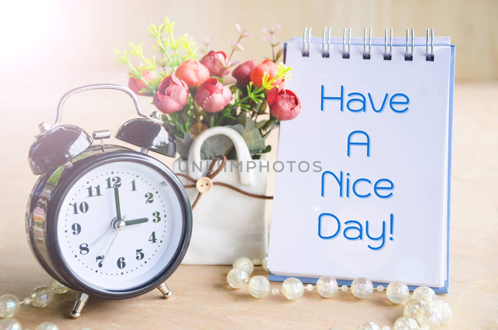 Have a nice day. On diary with flower cup and alarm clock on wooden background.