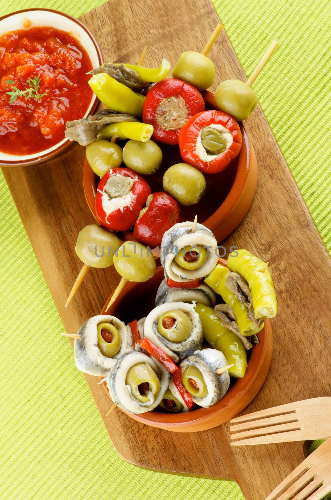 Delicious Spanish Snacks with Stuffed Small Peppers, Anchovies, Green Olives and Tomatoes Sauce with Bread Sticks in Various Bowls closeup on Green Napkin. Top View