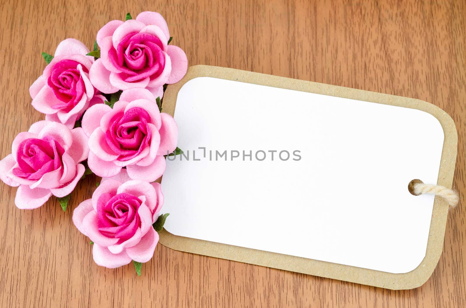 Blank paper tag and pink roses on wooden background for your text.