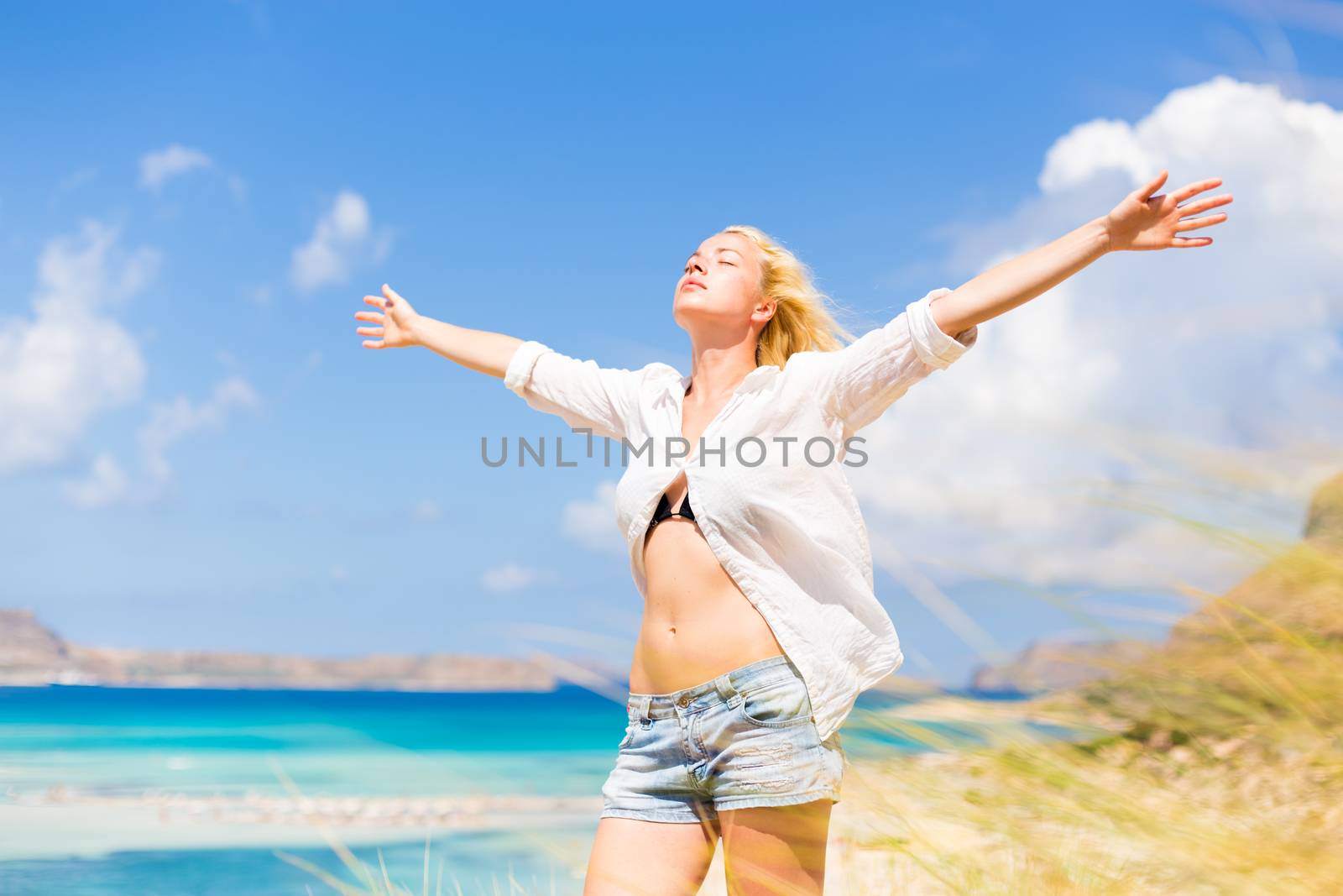 Relaxed woman enjoying freedom and life an a beautiful sandy beach.  Young lady raising arms, feeling free, relaxed and happy. Concept of freedom, happiness, enjoyment and well being.