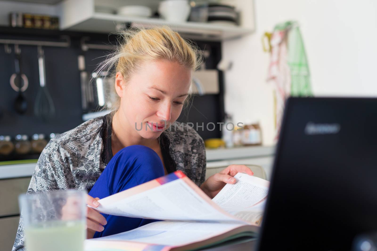 Female freelancer in her casual home clothing working remotly from her dining table in the morning. Home kitchen in the background.