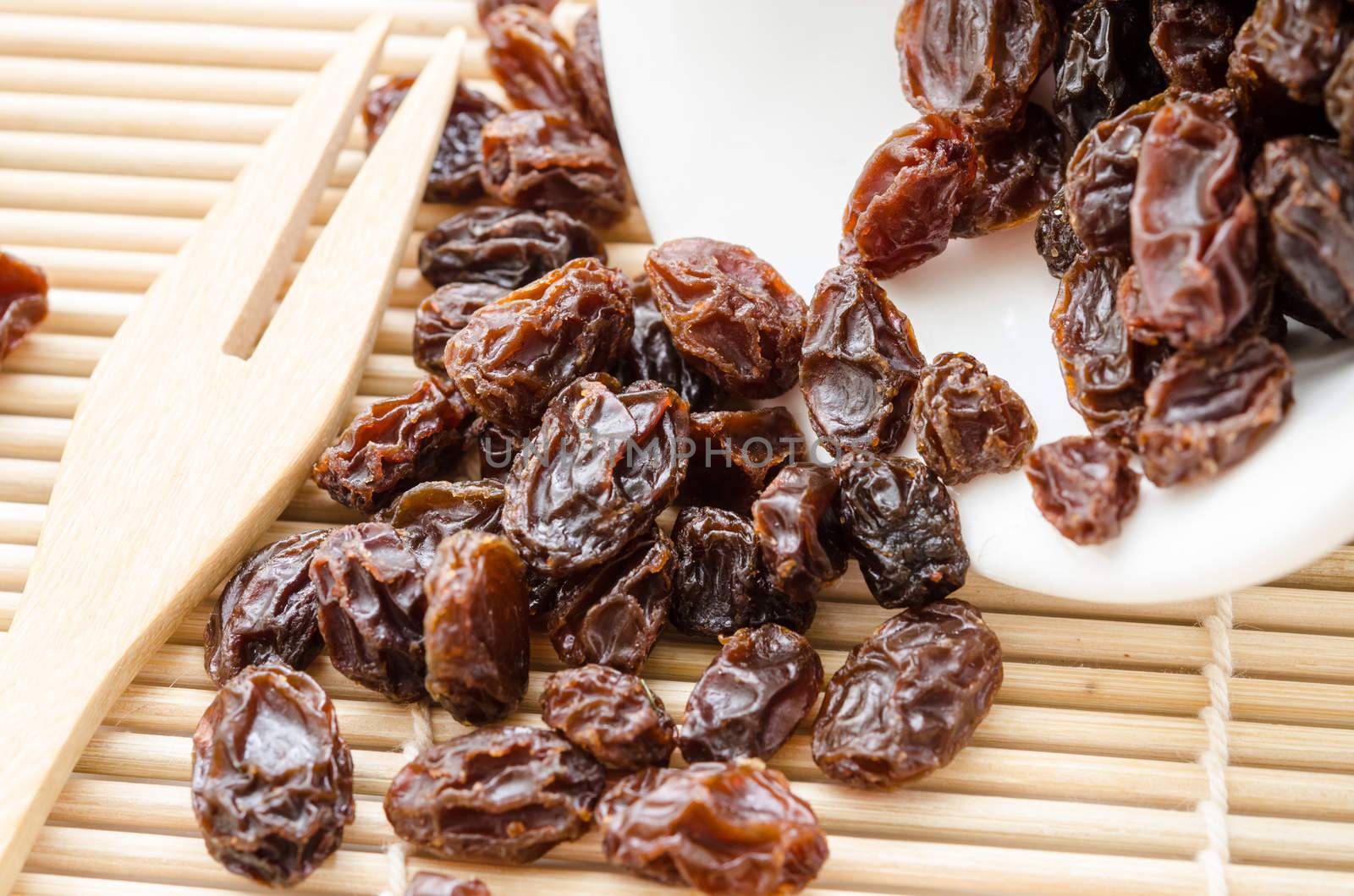 Raisin on white cup on wooden spoon fork on wooden mat background.