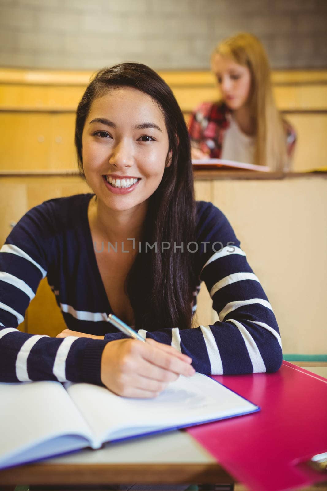 Smiling student writing on notebook by Wavebreakmedia