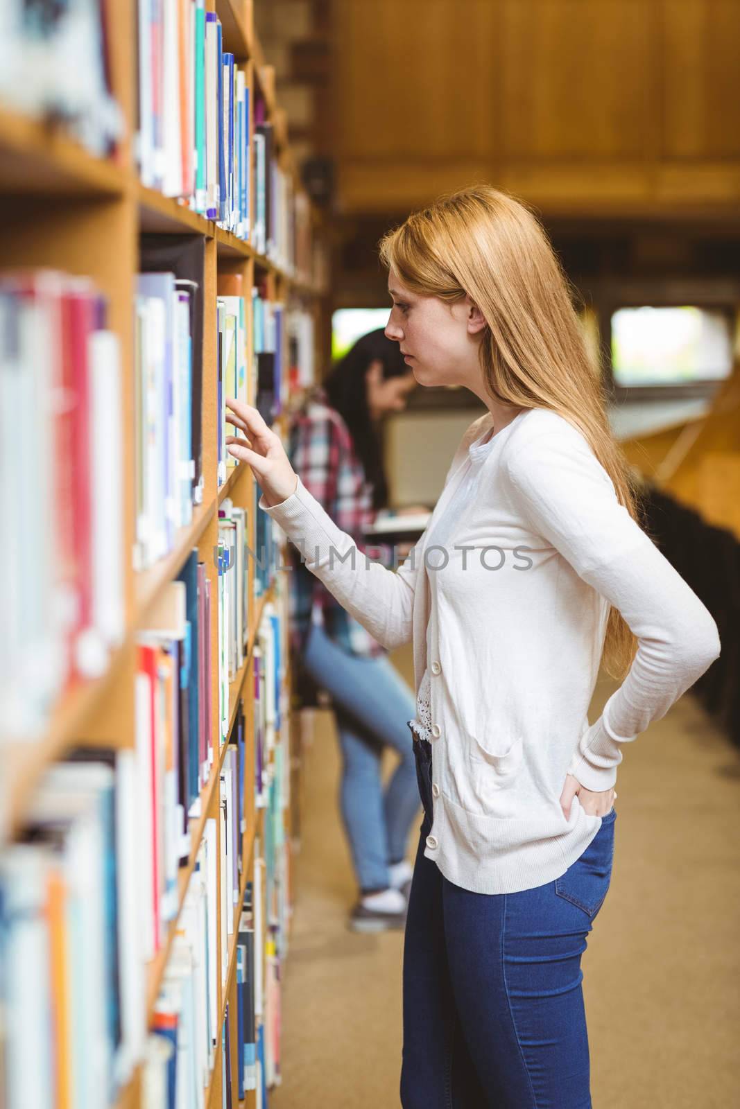Blond student looking for book in library shelves at the university