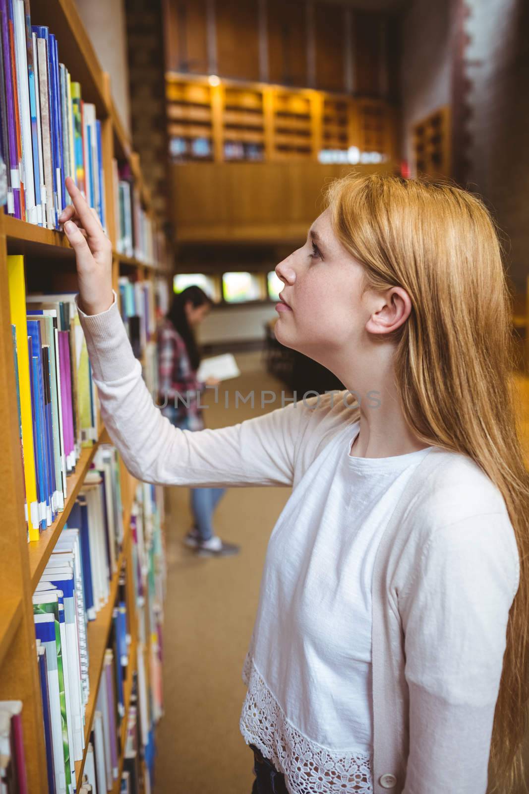 Blond student looking for book in library shelves at the university