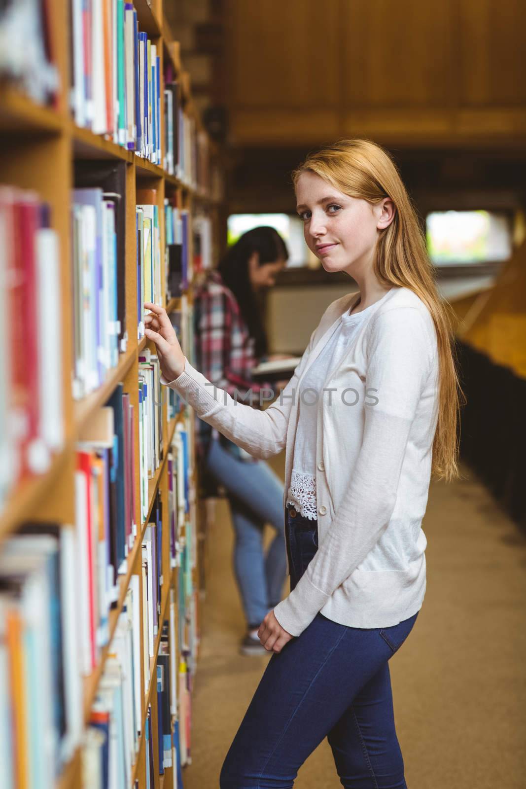Blond student looking for book in library shelves at the university