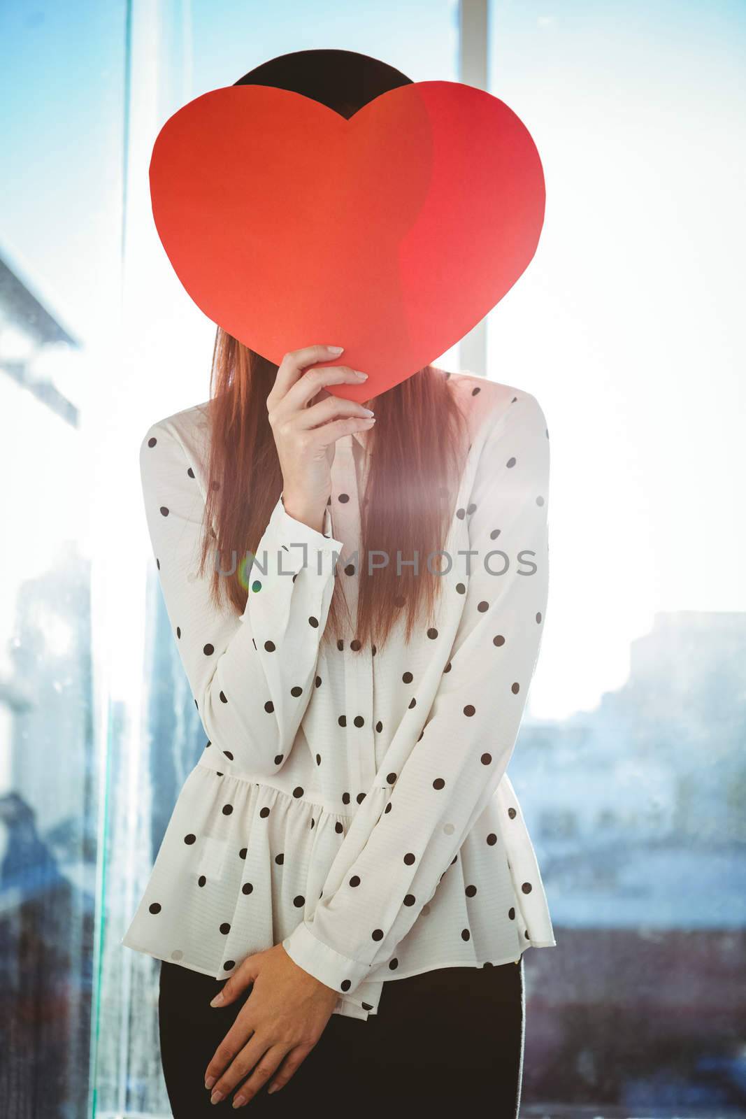 Attractive hipster woman behind a red heart in a bright room