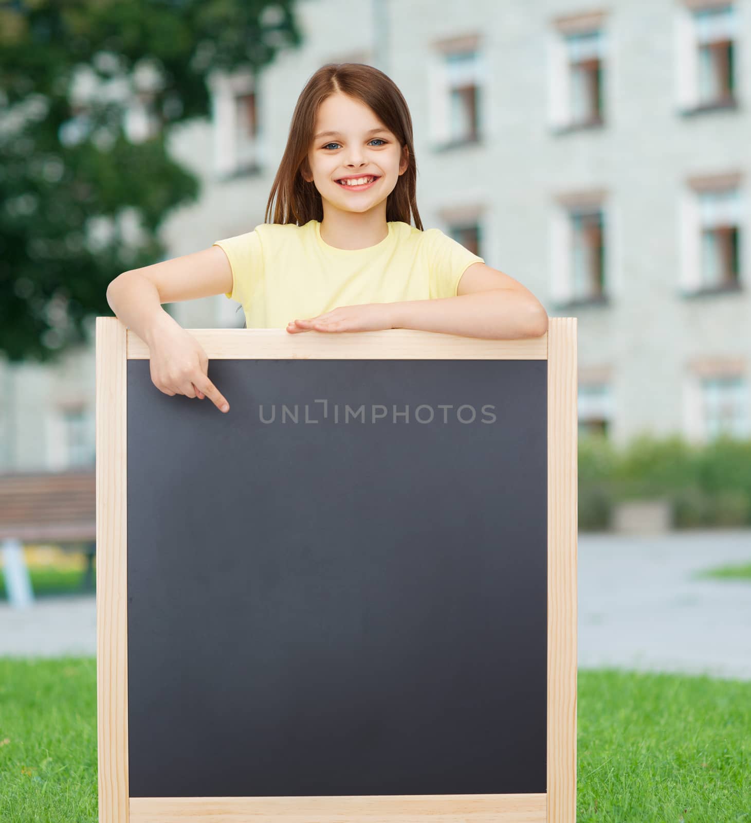 people, advertisement and education concept - happy little girl pointing finger to blackboard