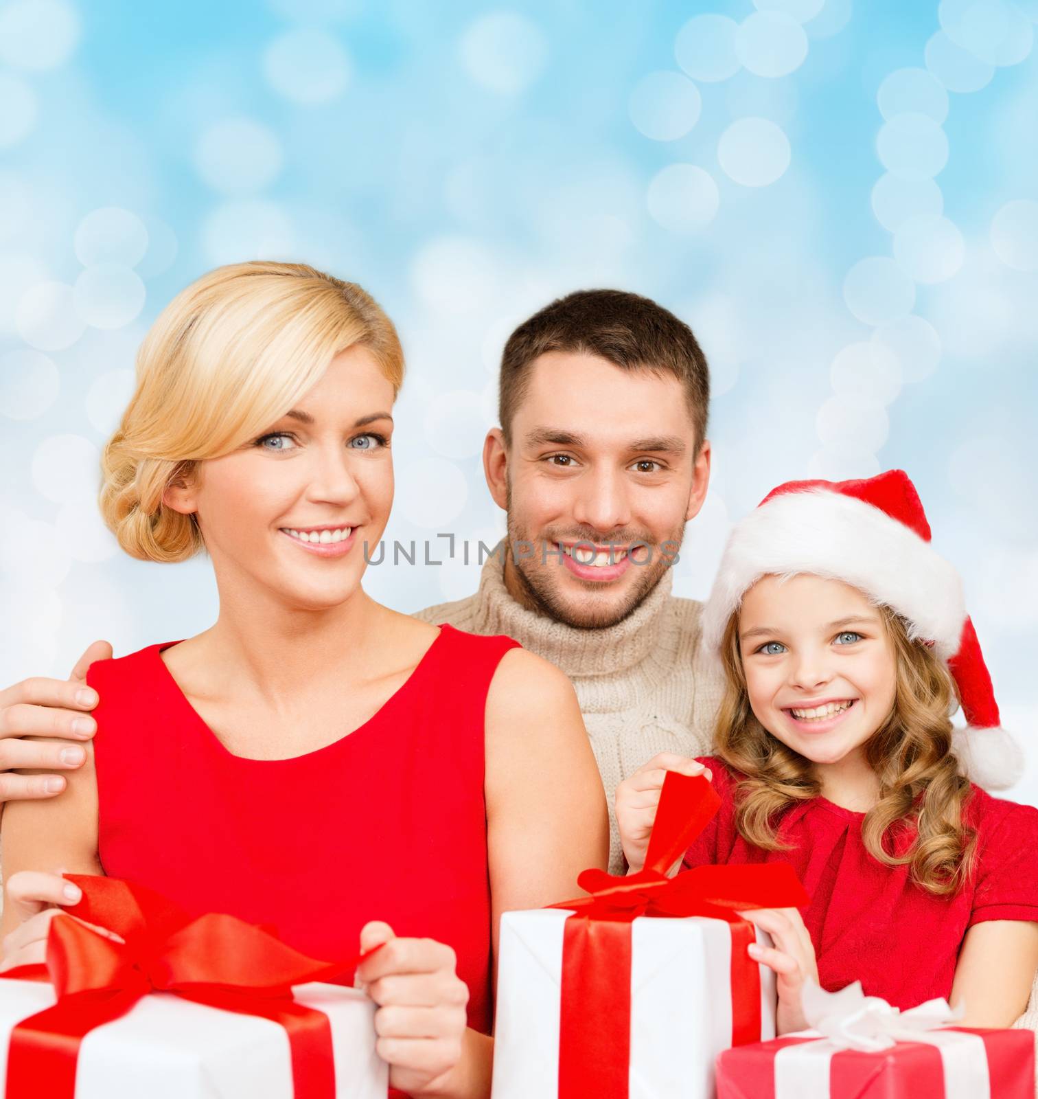 christmas, holidays, family and people concept - happy mother, father and little girl in santa helper hat with gift boxes over blue lights background