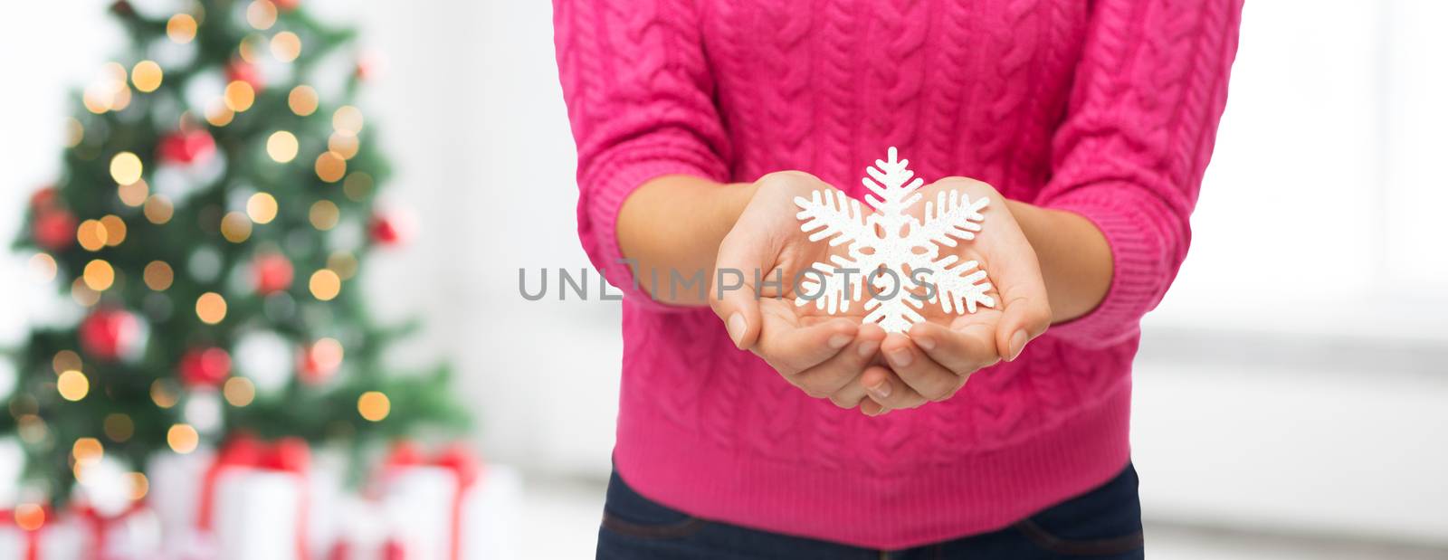 winter, holidays and people concept - close up of woman in pink sweater holding snowflake decoration over living room with christmas tree lights background