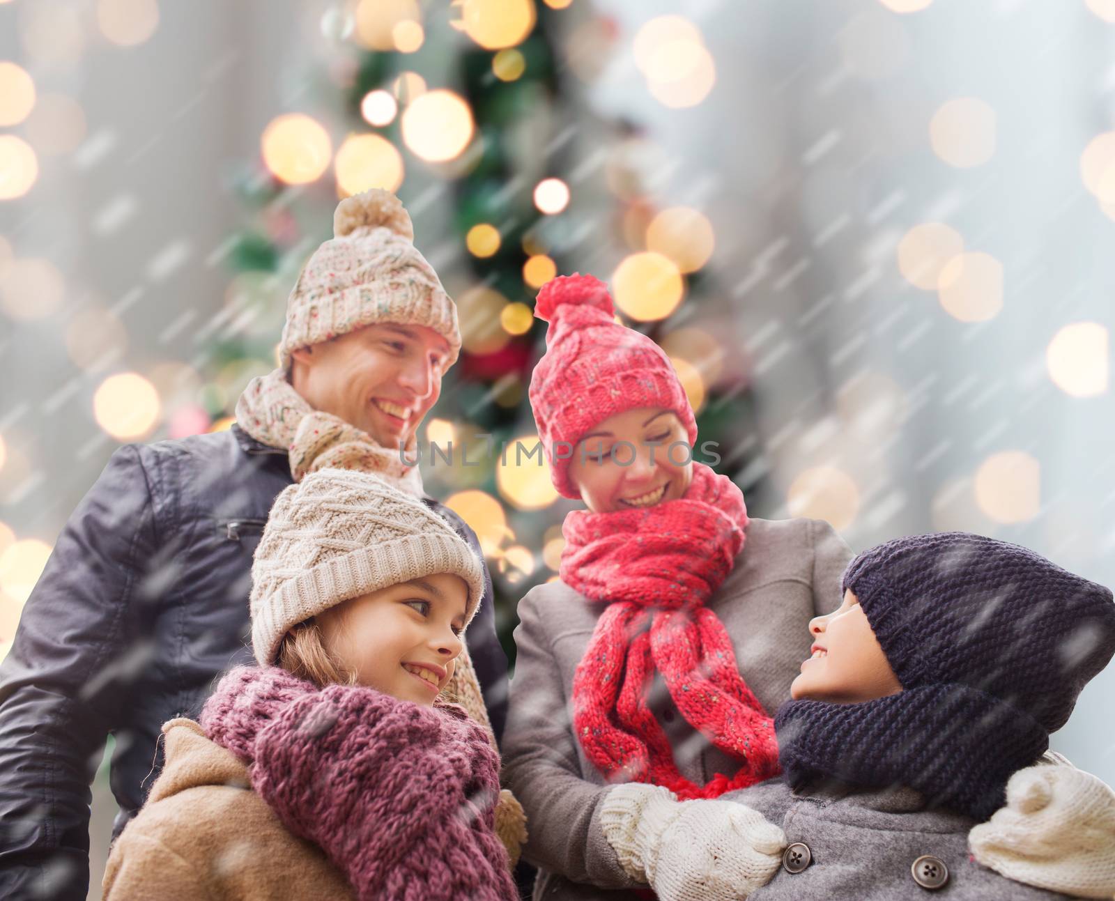 family, childhood, season, holidays and people concept - happy family in winter clothes over christmas tree lights background