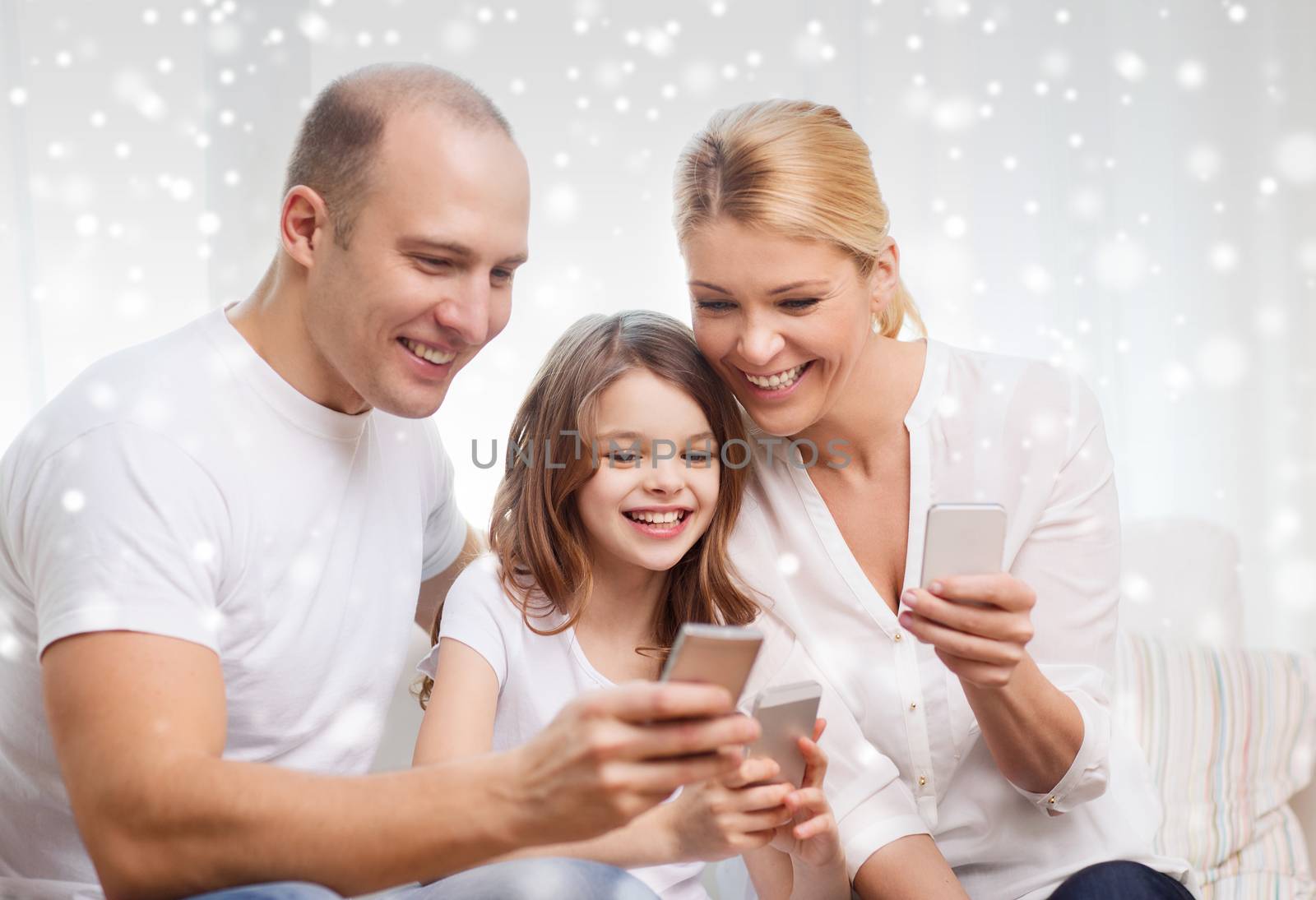 family, home, technology and people concept - smiling mother, father and little girl with smartphones over snowflakes background