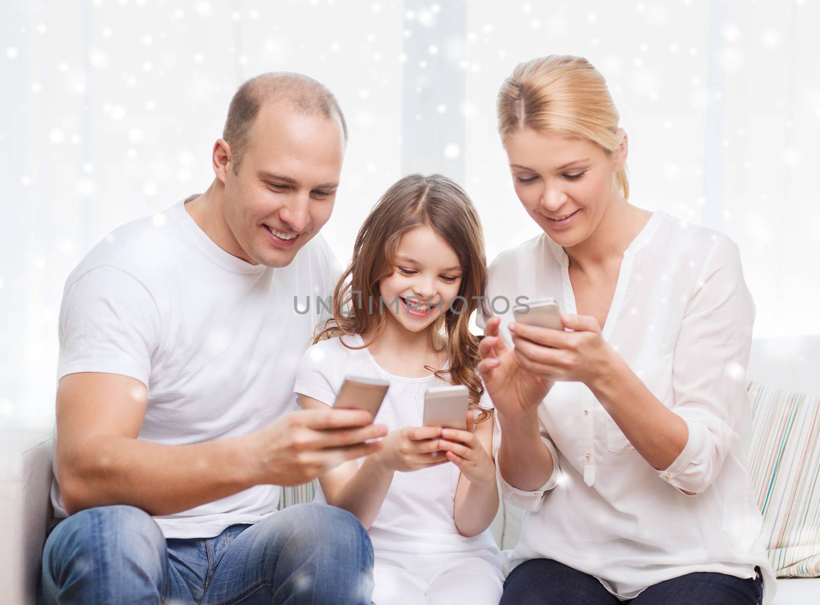 family, home, technology and people concept - smiling mother, father and little girl with smartphones over snowflakes background