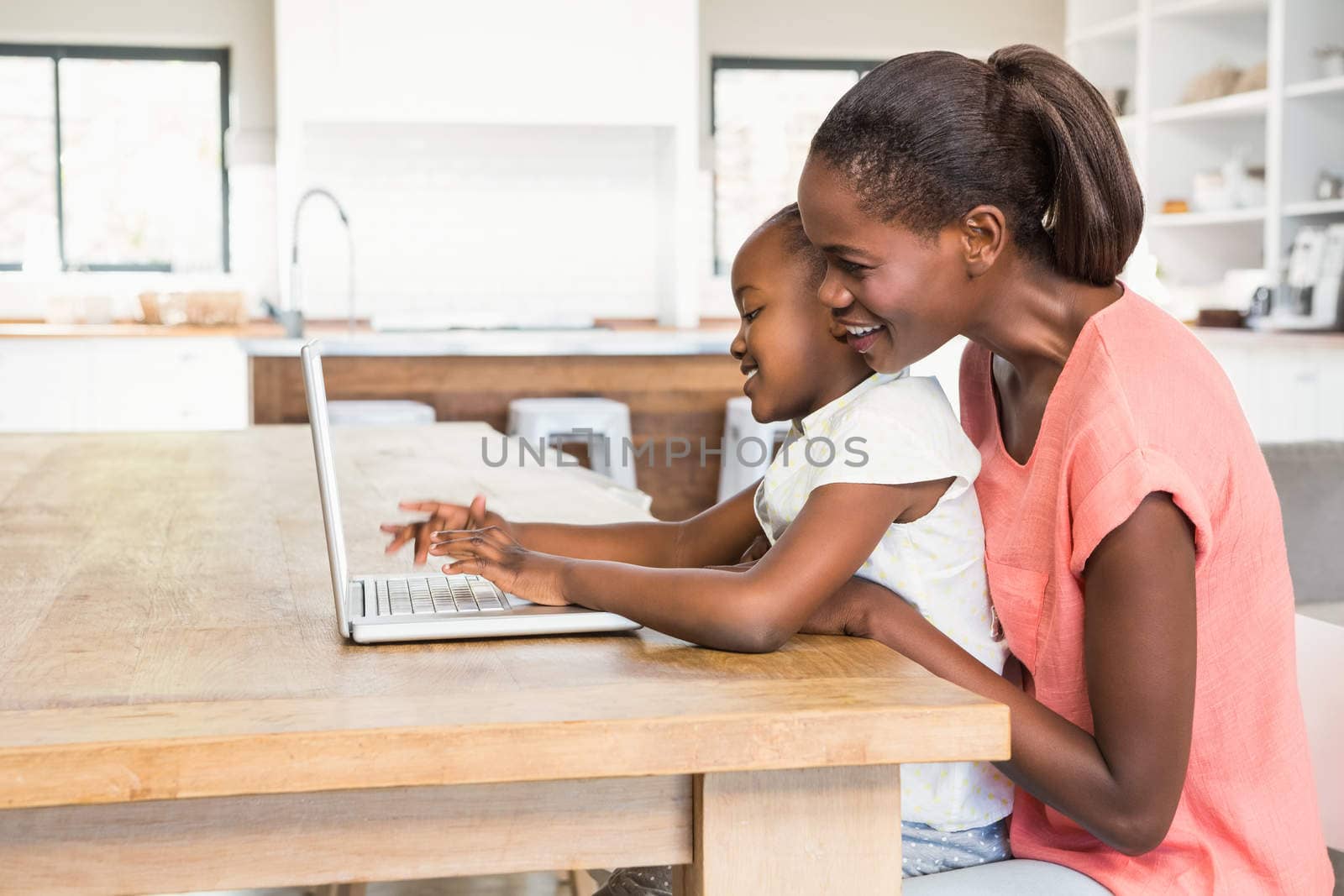 Cute daughter using laptop at desk with mother in living room