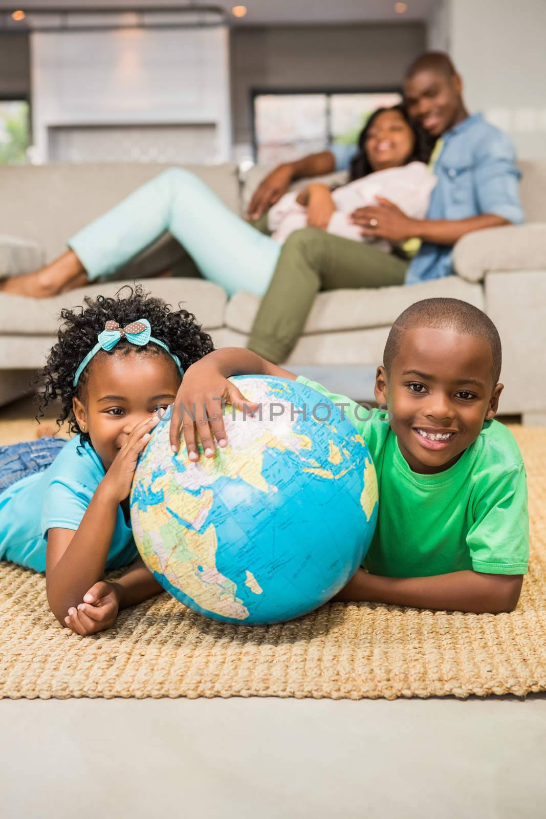 Happy siblings lying on the floor holding globe in the living room 