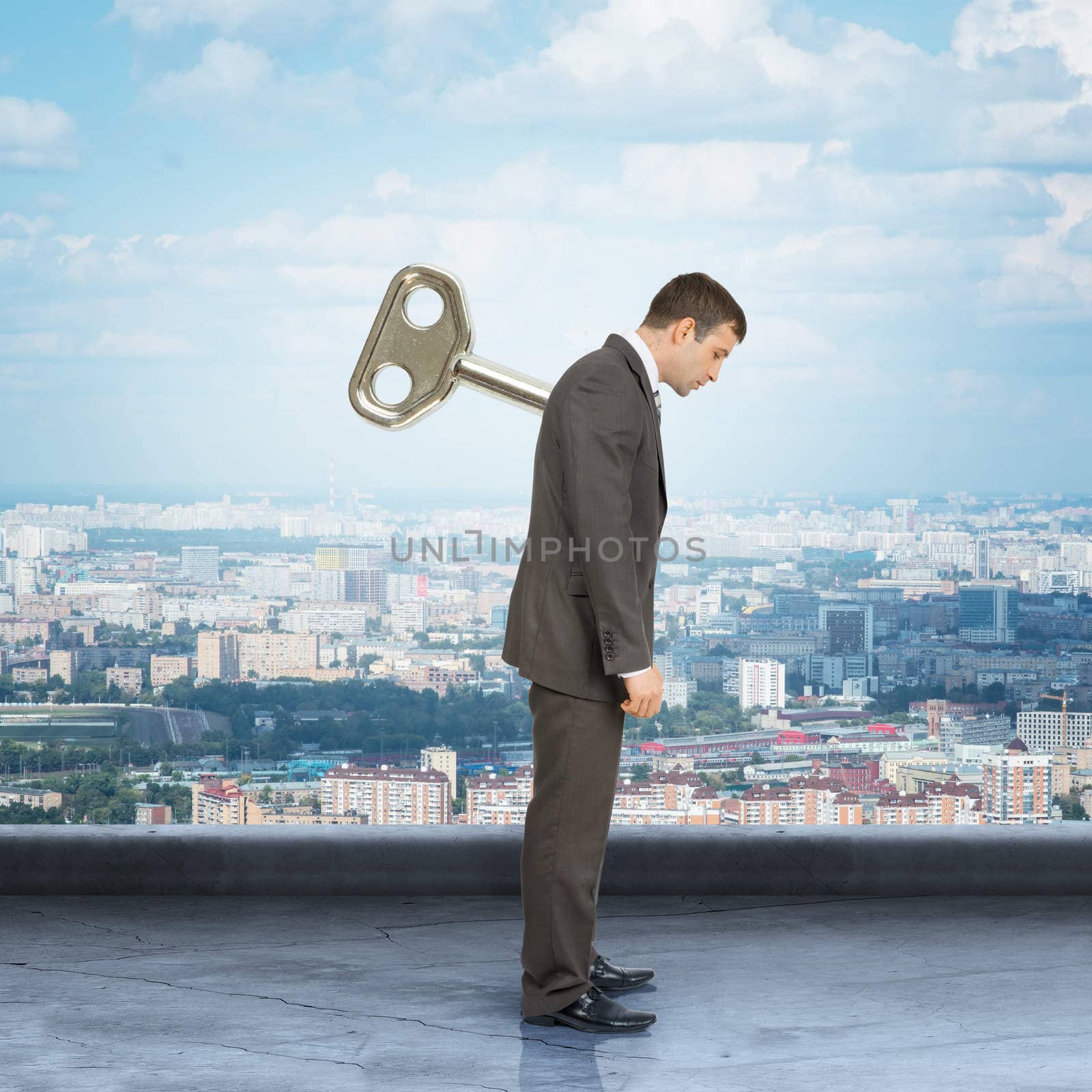Businessman looking down with key in back with city background
