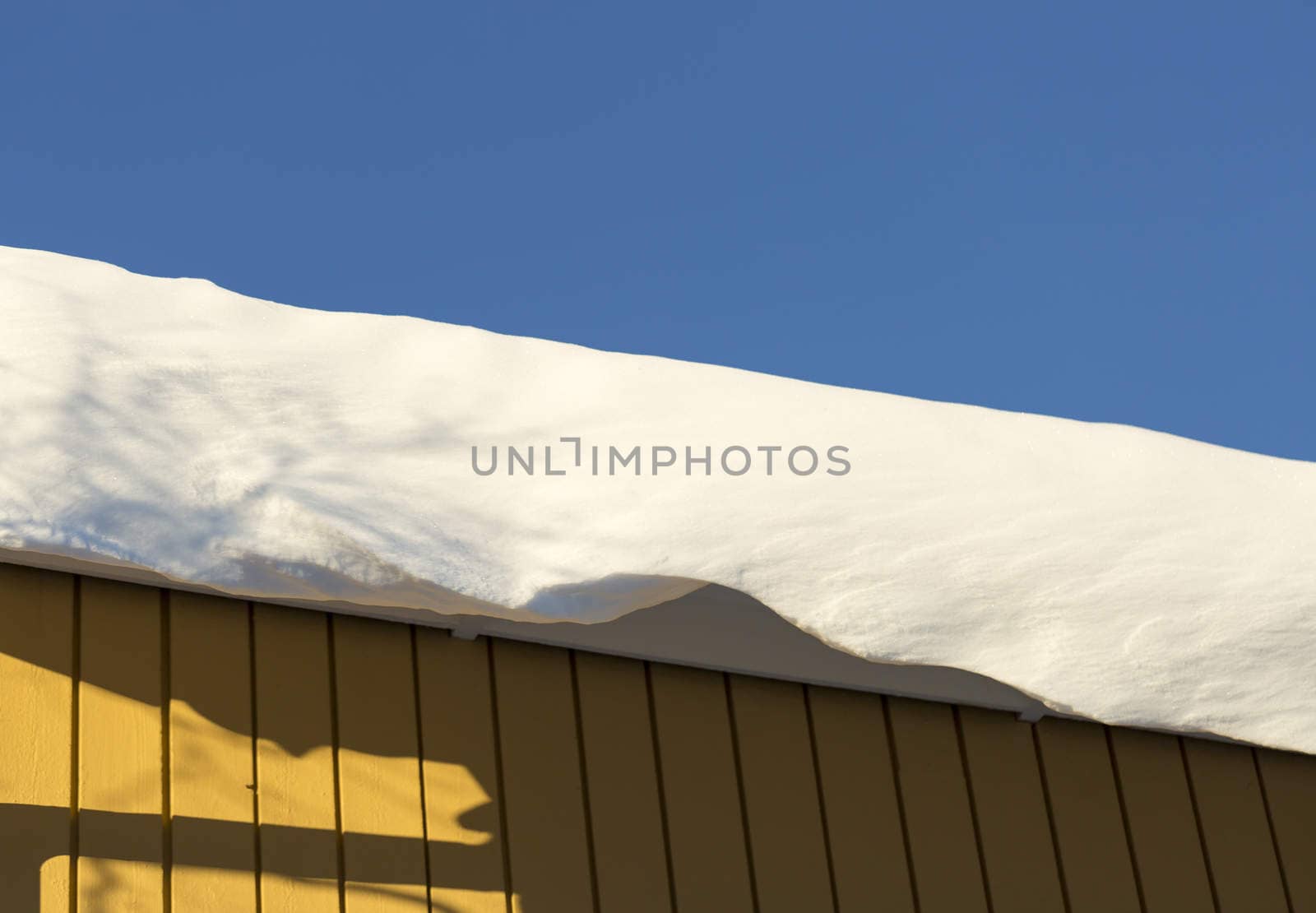 Snow Sheet Hanging from Roof with a clear blue sky behind it.