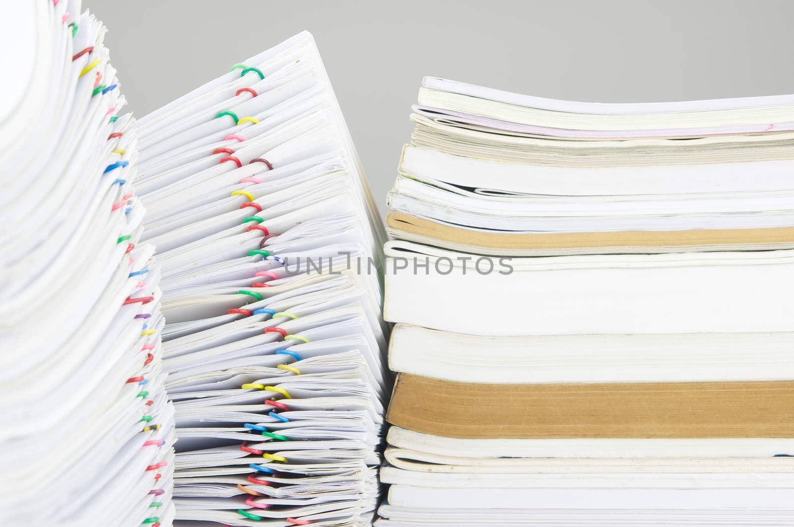 Colorful paper clip with pile of report place on finance account have blur pile of paperwork as foreground and blur book as background.