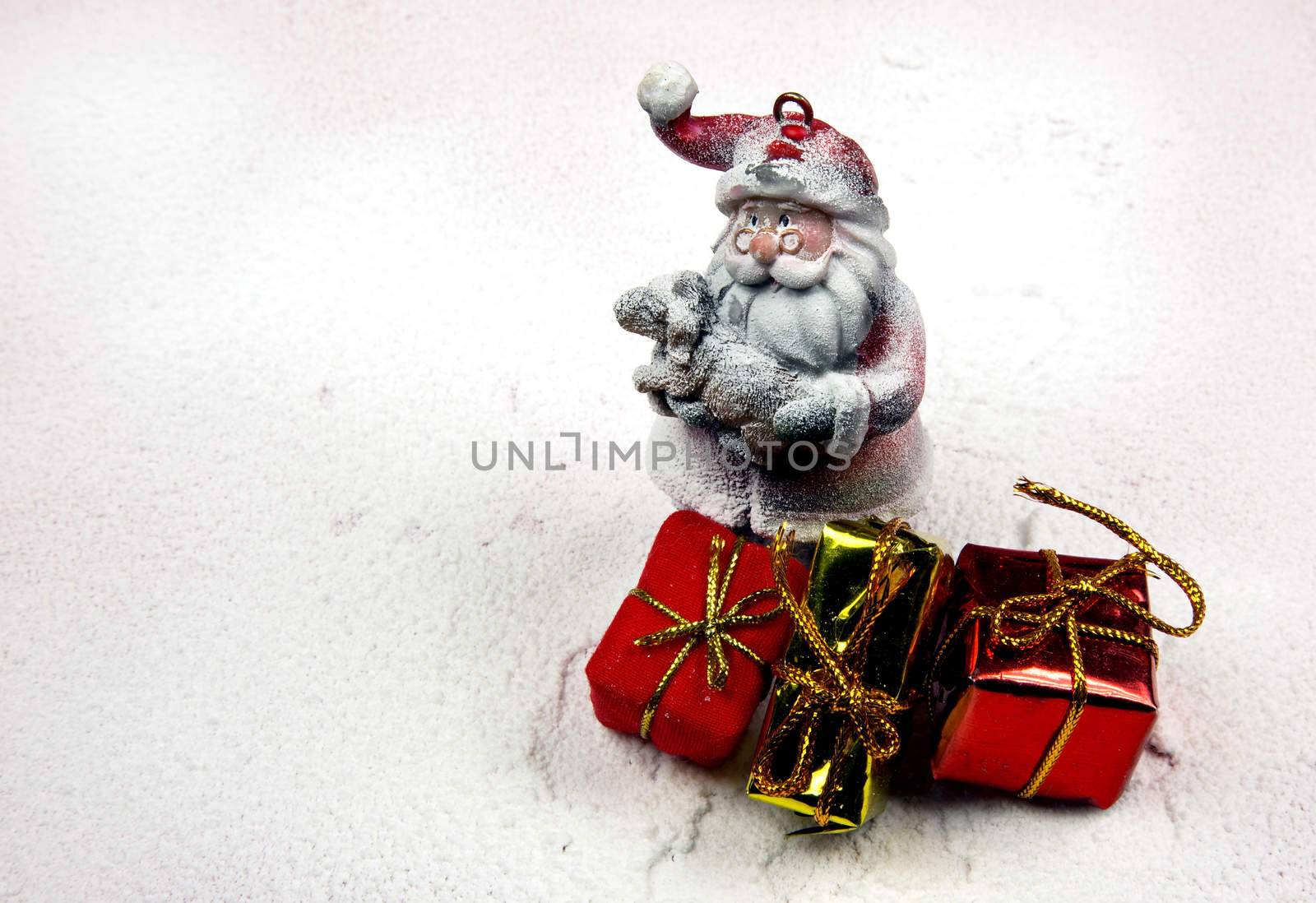 Christmas decoration, snowy figure of Santa Claus holding in his arms a little lamb and three decorative gifts .Horizontal view.