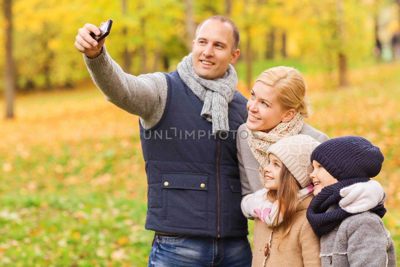 family, childhood, season, technology and people concept - happy family taking selfie with smartphone in autumn park