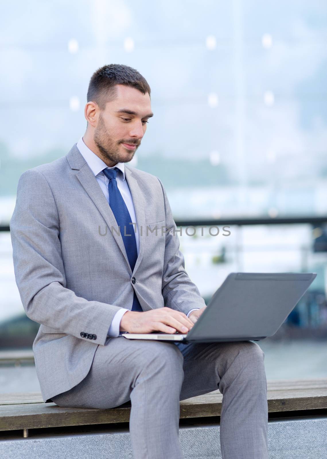 business, education, technology and people concept - businessman working with laptop computer on city street