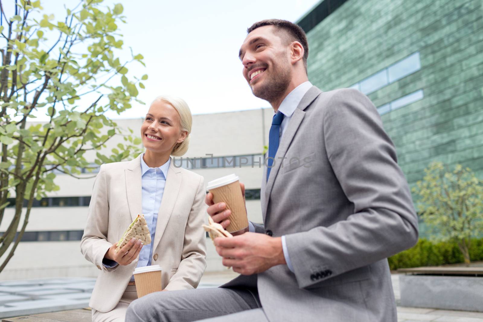 business, partnership, food, drinks and people concept - smiling businessmen with paper cups standing over office building