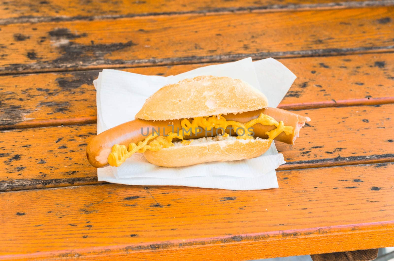 Sausage with mustard on buns. The sausage is on a brown wooden table.