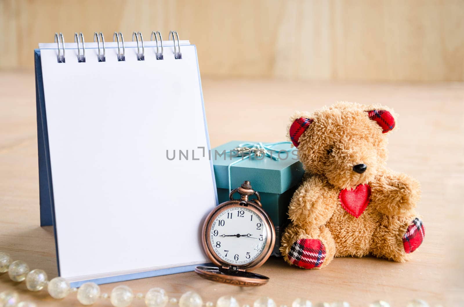 Open diary and vintage pocket watch with brown bear doll on wooden background.