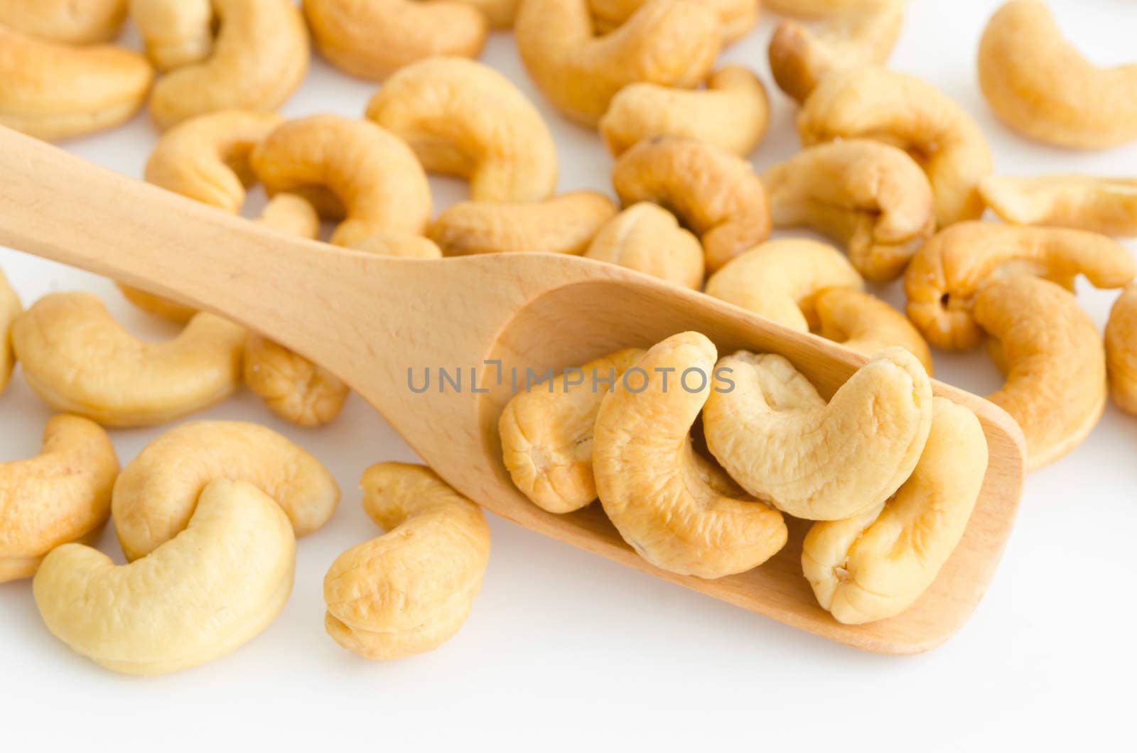 Cashew nuts in wooden spoon on white background.