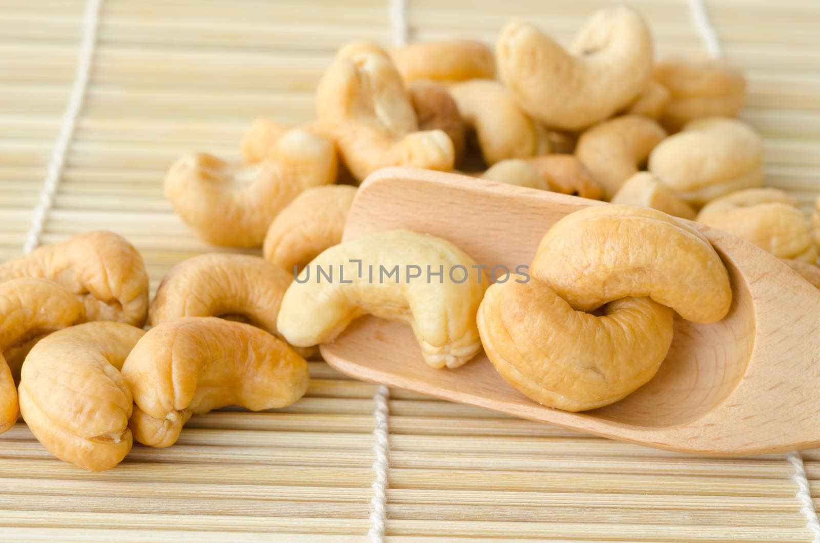 Close up cashew nuts in wooden spoon on mat wooden.