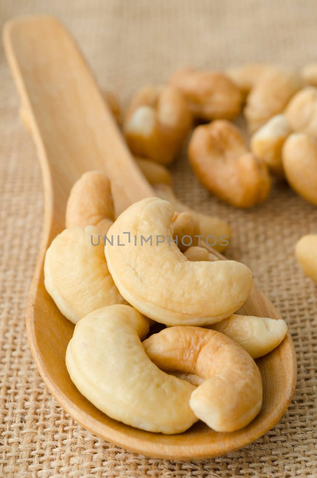 Cashew nuts in wooden spoon on sack background.