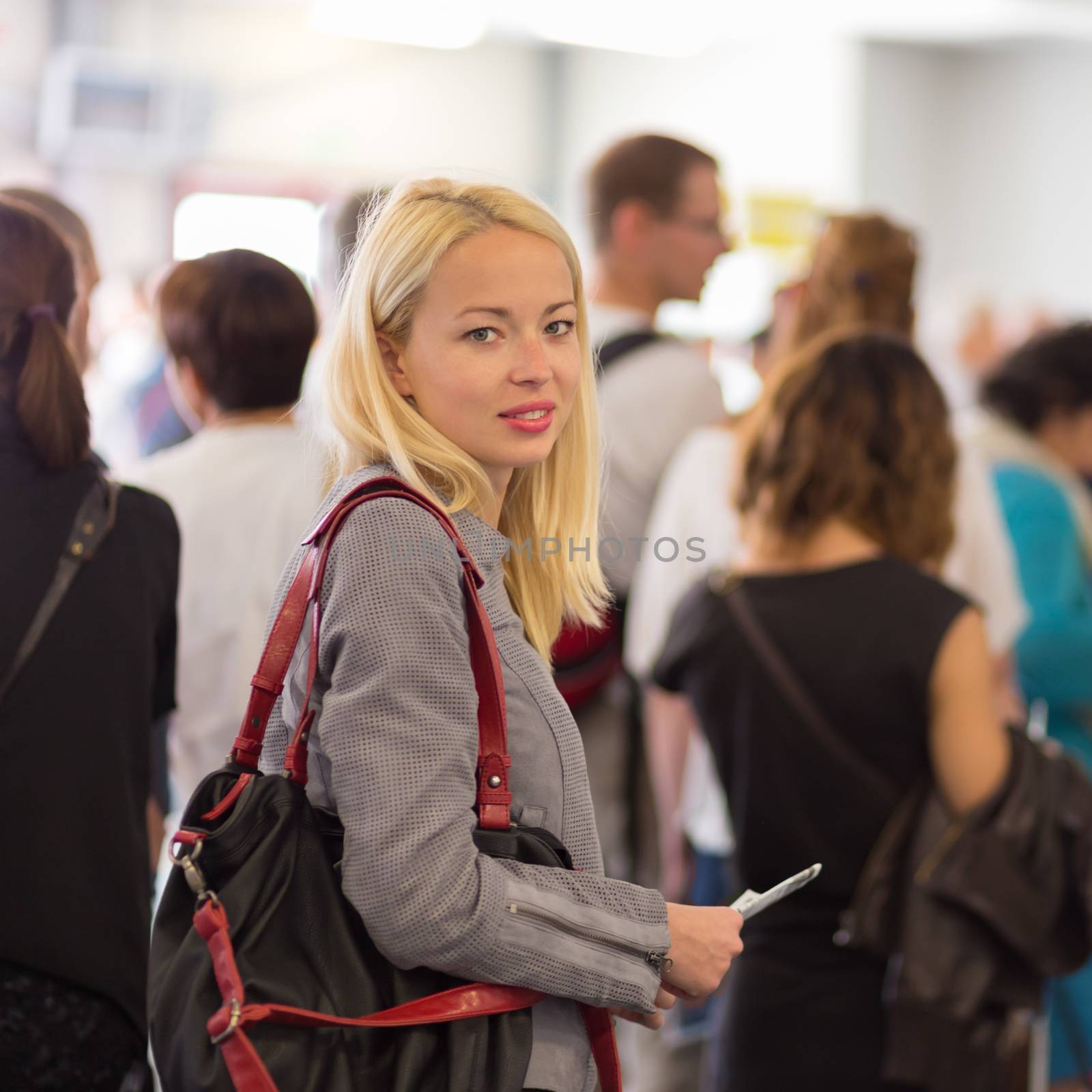 Young blond caucsian woman waiting in line with plain ticket in her hands. Lady standing in a long queue to board a plane.