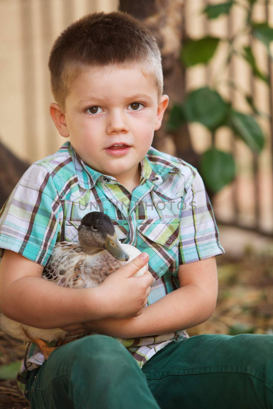Single smiling child holding a duck outdoors