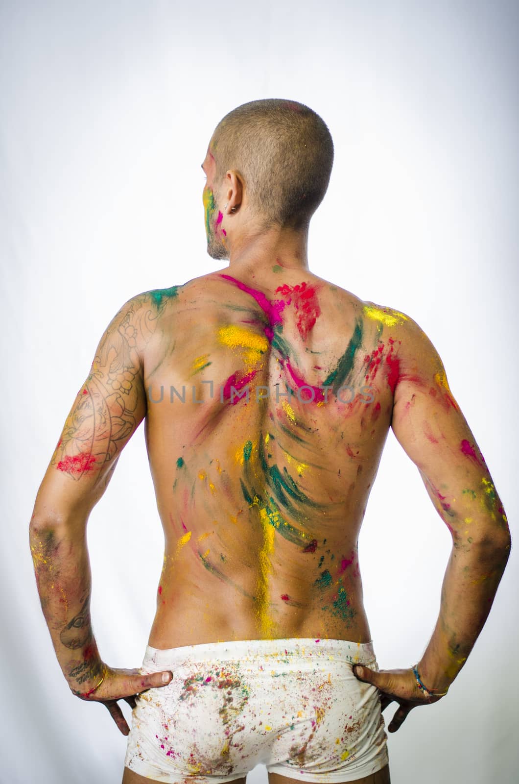 Handsome young man seen from the back with skin all painted with Holi colors
