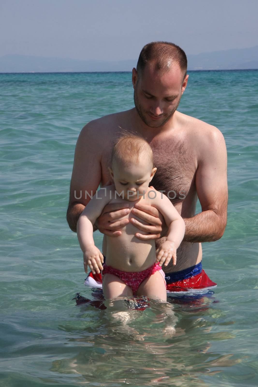 Father halps his baby daughter to to feel good in the sea water