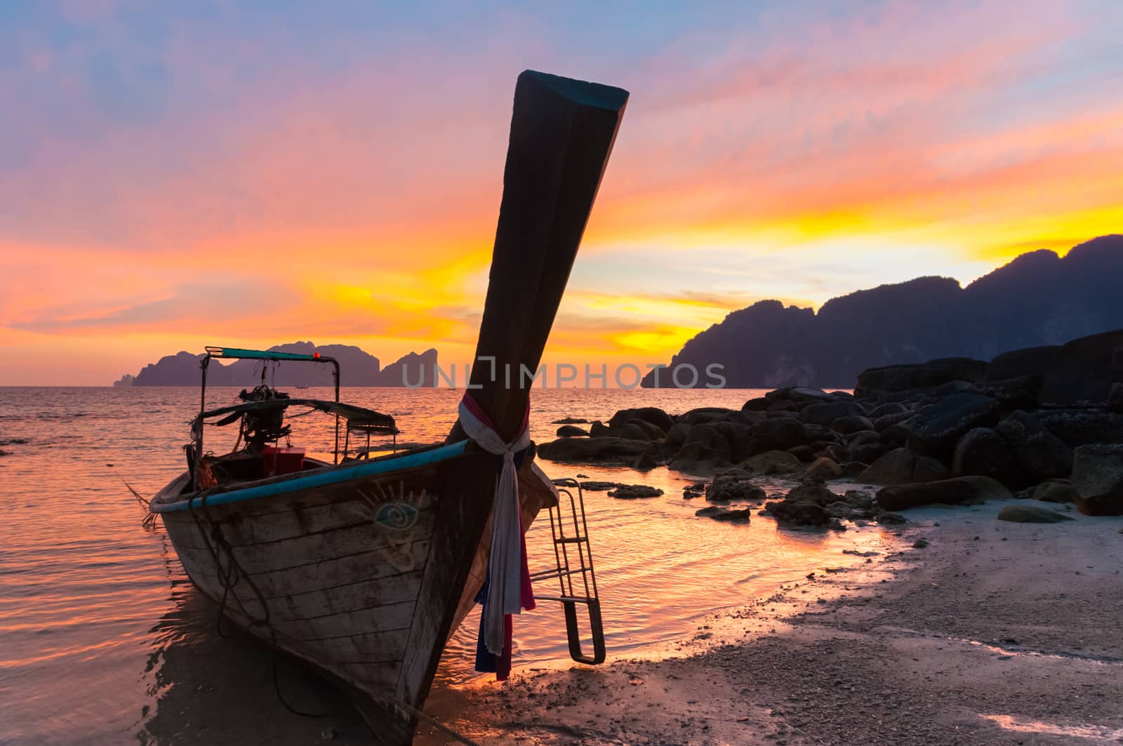 Traditional thai wooden longtail boat on beach of Phi-Phi Don island in sunset. Silhouette of famous Phi Phi Lee island in background. Thailand, Krabi province.
